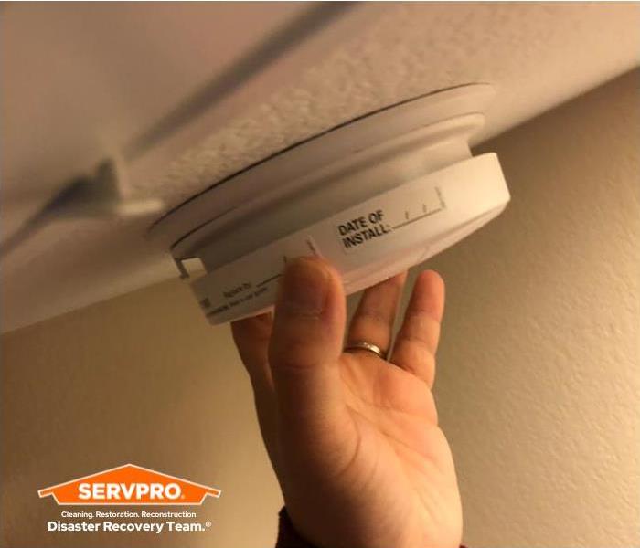 photo of a man's hand setting up a smoke alarm in ceiling of a room
